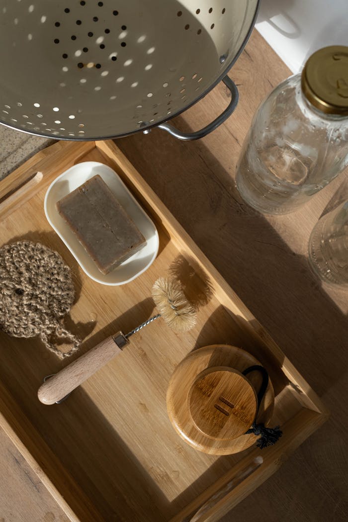 Flatlay of rustic eco-friendly kitchen utensils on a wooden tray with sunlight.