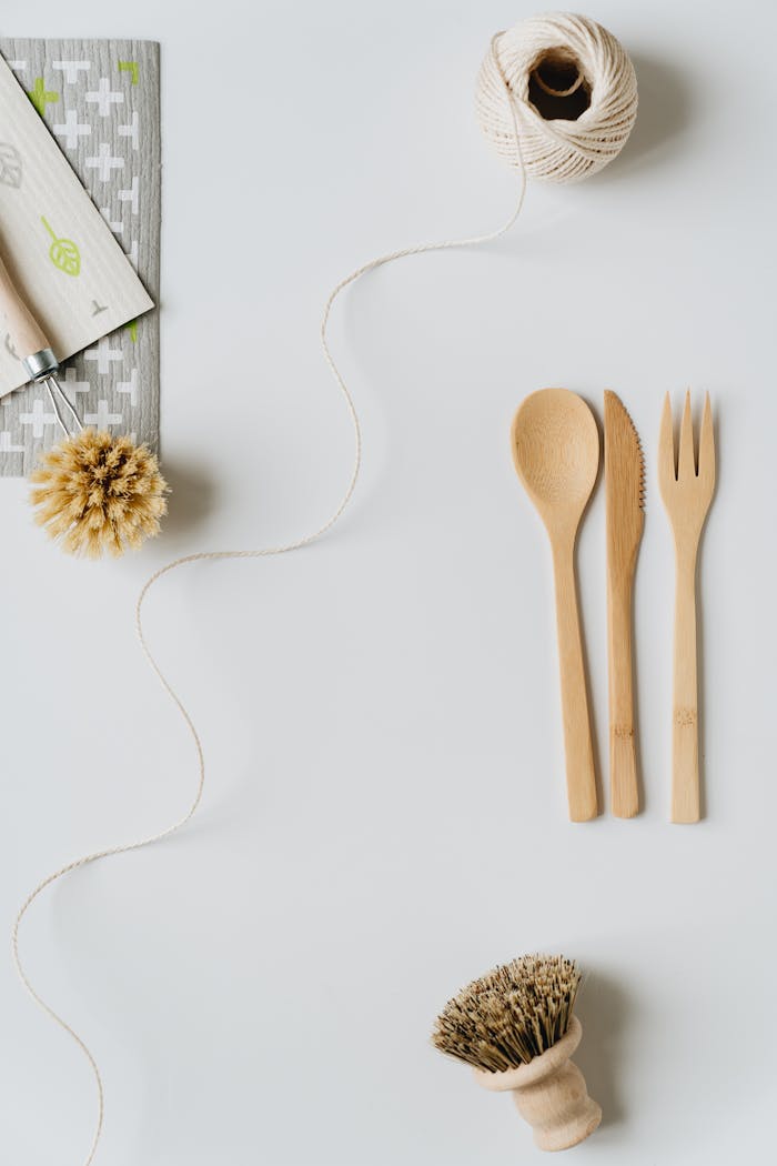 Flat lay of eco-friendly kitchen utensils including wooden cutlery and a cleaning brush on a white background.